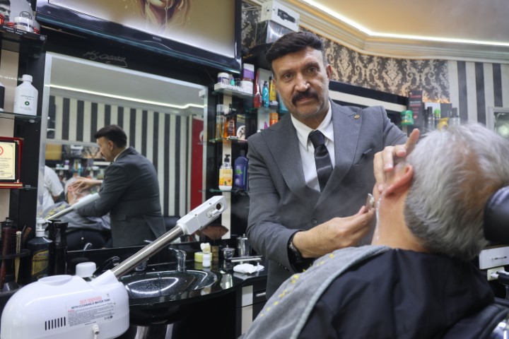 Mesleğine olan ciddiyetini kaybetmeyen berber müşterilerini takım elbiseyle tıraş ediyor